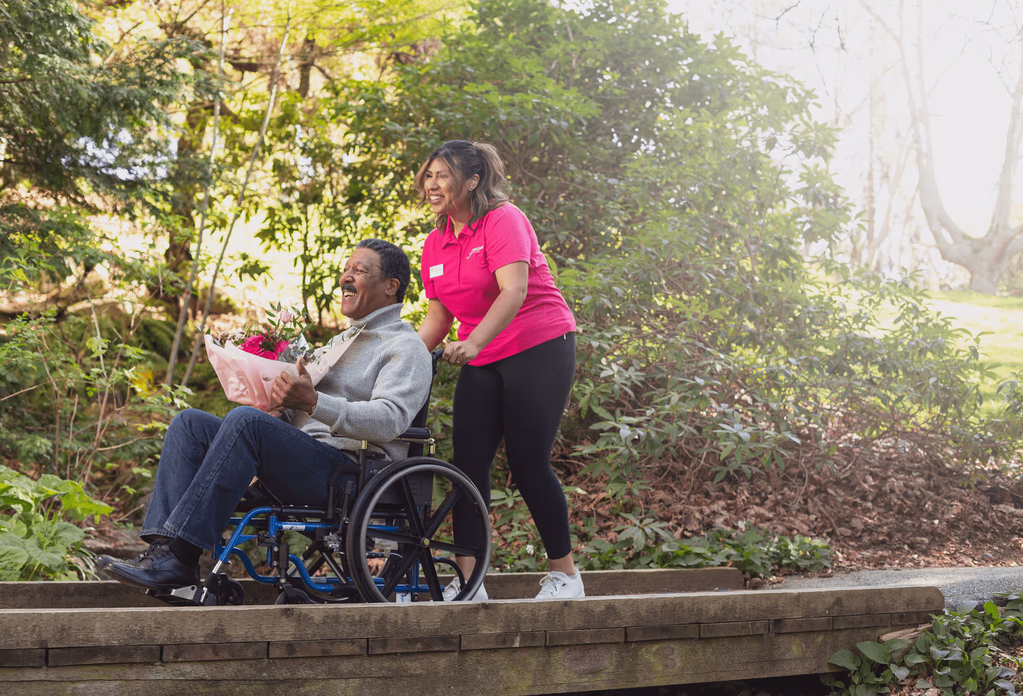 A man in a wheelchair is being pushed by a woman in a pink shirt.